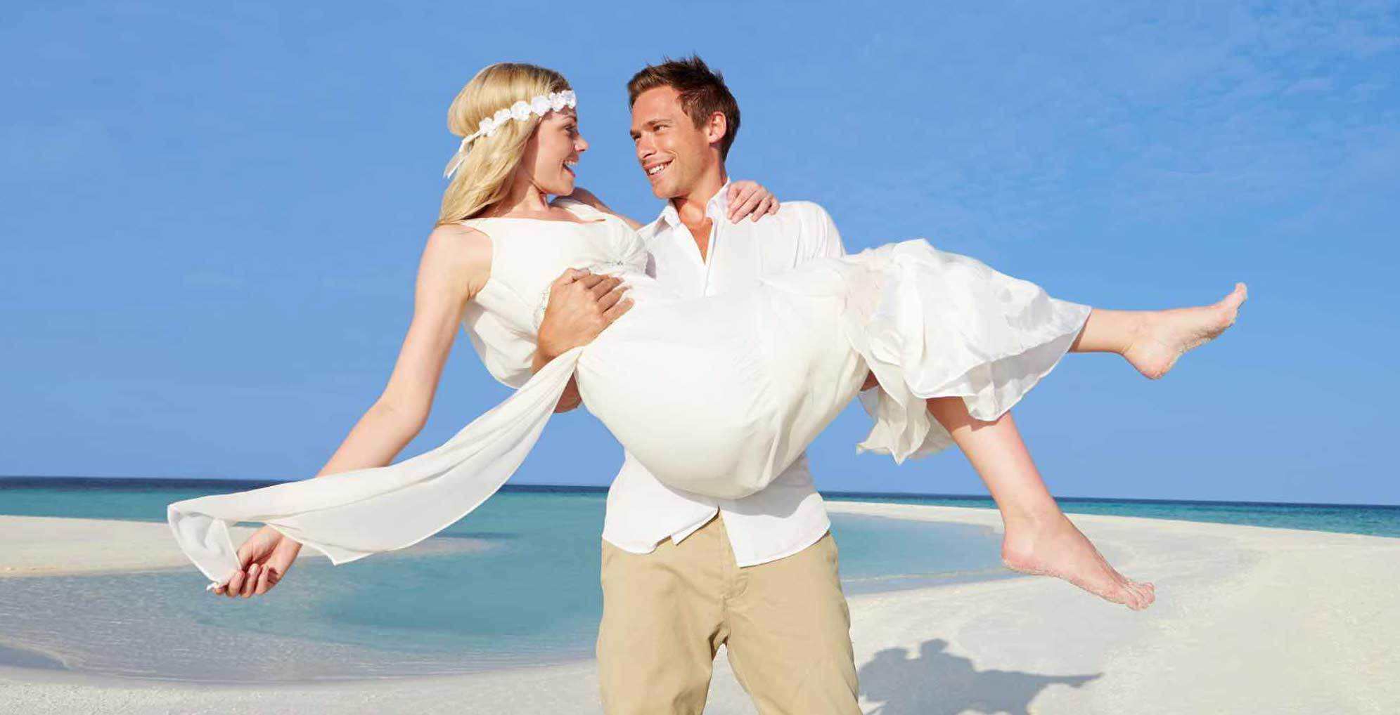 groom carries bride at beach